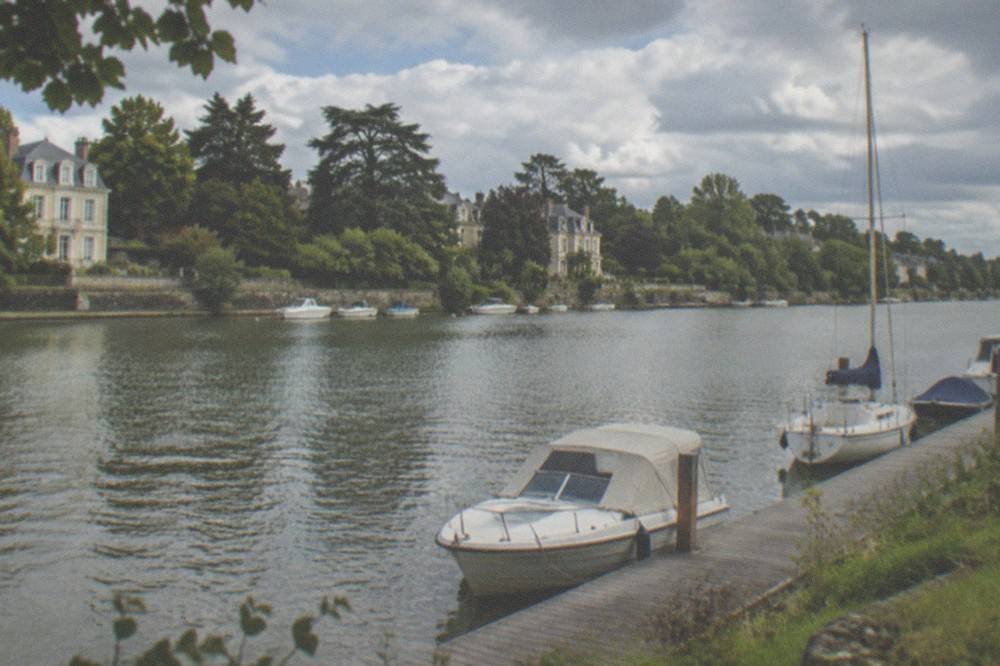 Trees along the banks of the Erdre river in Nantes with pleasure boats moored at a wooden pontoon