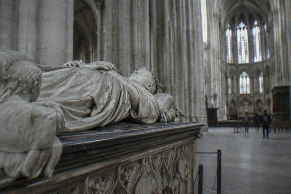 Detail of a carved stone tomb with reclining marble figures in a cathedral nave
