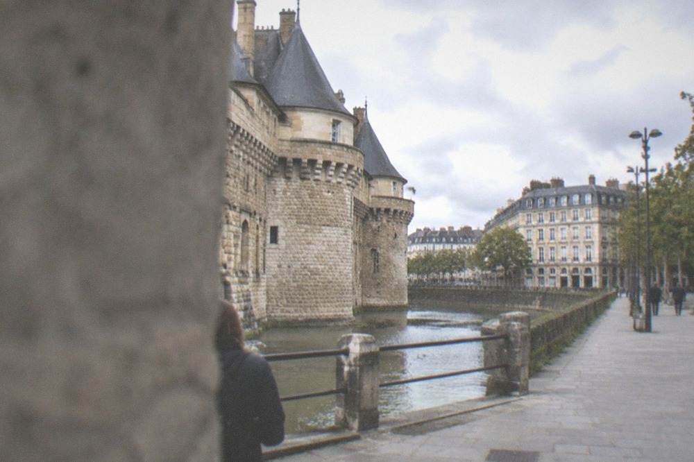 A stone fortress with towers and a moat beside a city square in Nantes