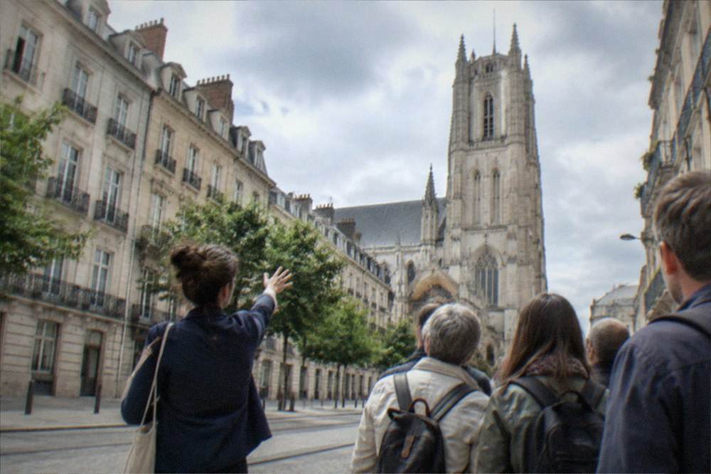 A guide leading a small group of visitors along a historic Nantes street towards a cathedral tower