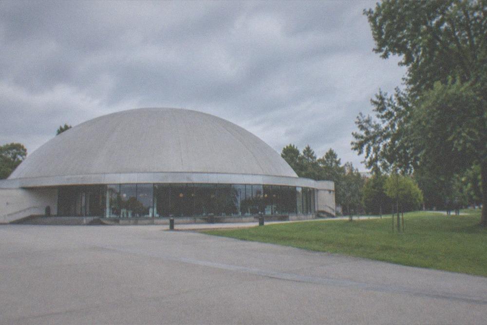A domed planetarium building beside a park in the evening