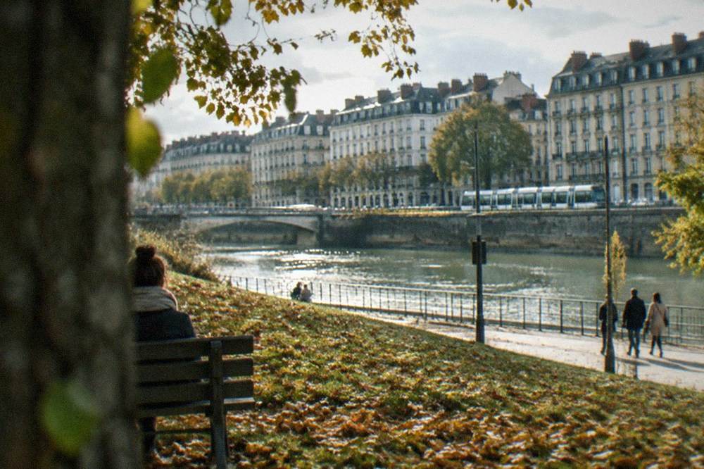 Autumn leaves covering a grassy slope beside a park bench in Nantes