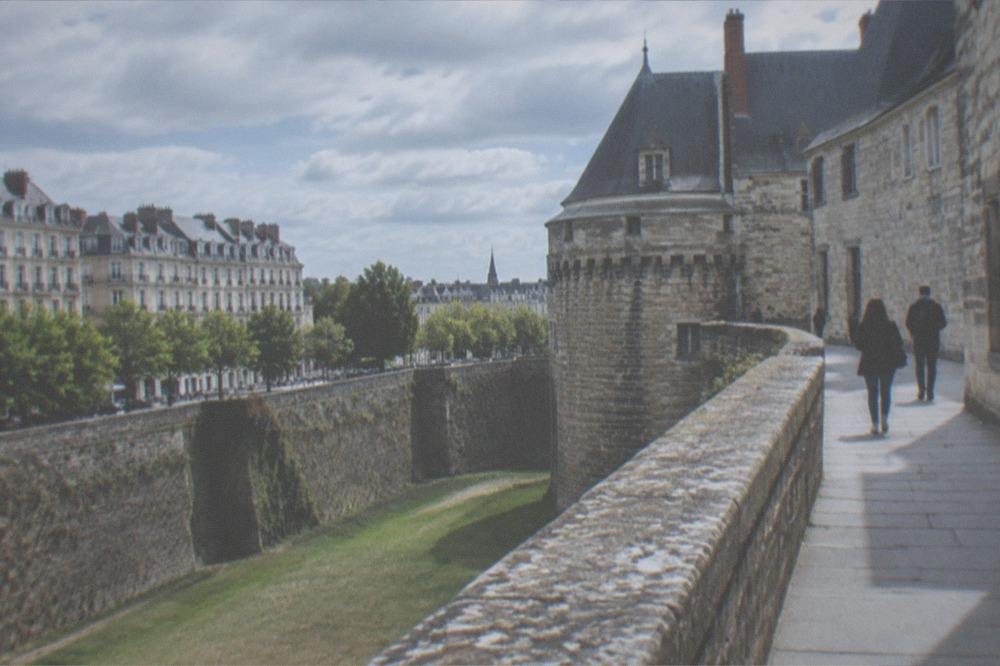A stone château wall and rampart walk beside a dry moat in Nantes