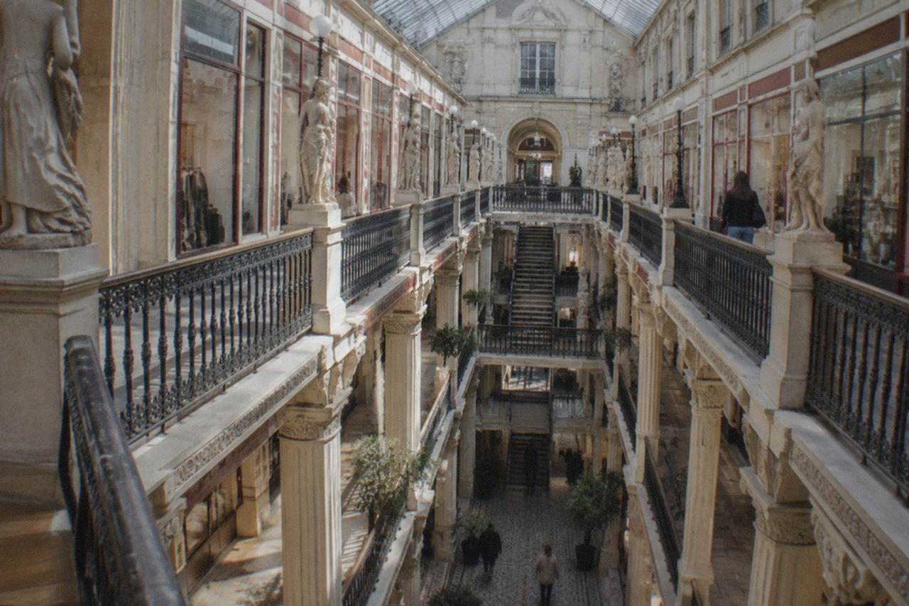 Sunlight falling through the glass roof of an elegant nineteenth-century shopping arcade lined with boutique storefronts