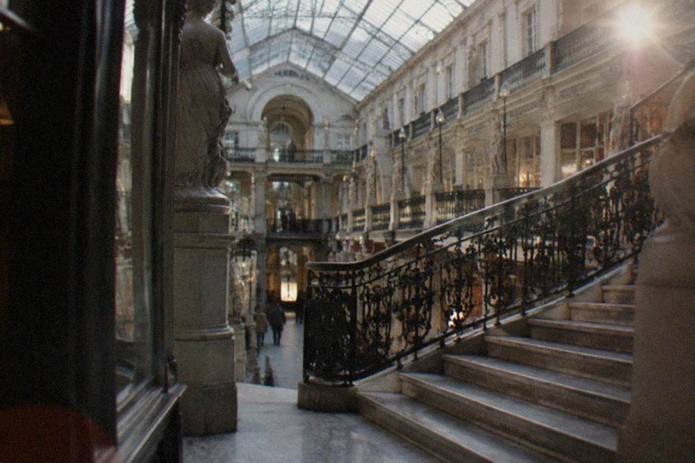 A marble staircase with an ornate wrought iron balustrade rising through the levels of a bright shopping arcade