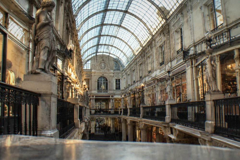 The curved glass canopy of a nineteenth-century arcade seen from below with iron ribs and daylight streaming through