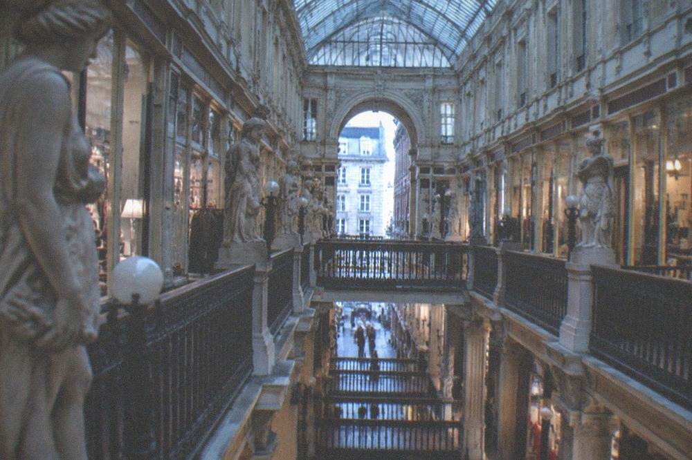 A long view down a covered shopping arcade with symmetric shopfronts and daylight at the far end