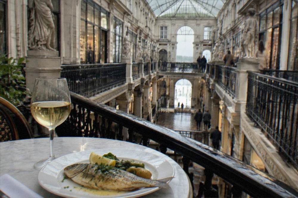 A glass of pale white wine and a plate of fresh river fish with butter sauce on a marble cafe table