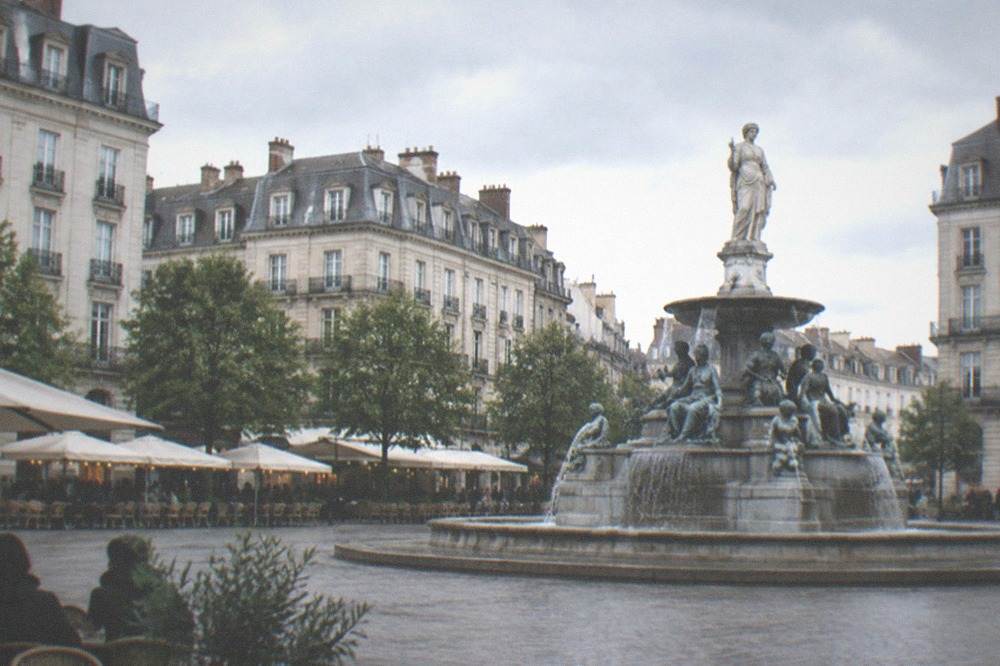 A fountain with sculpture at the centre of a classical square in Nantes with cafe terraces around the edge