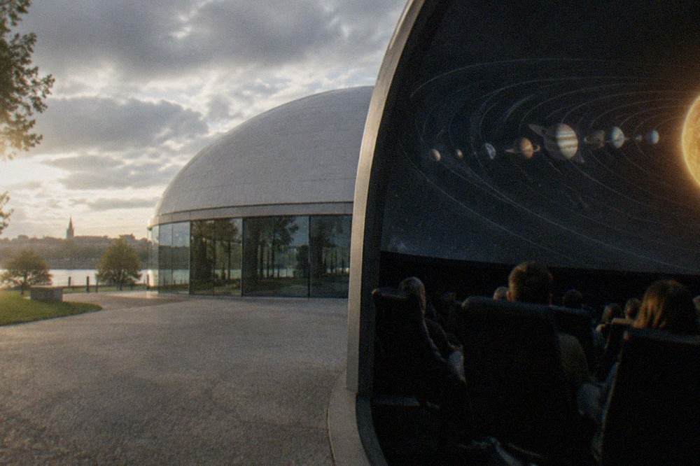 Visitors seated in reclining planetarium chairs watching a projected solar system on the dome above them