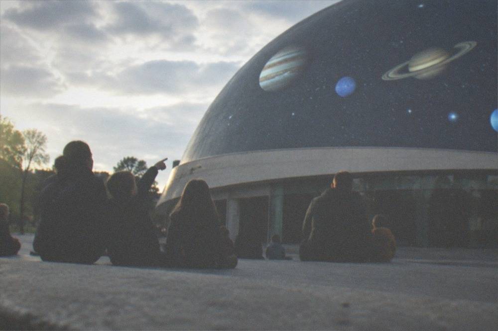 Children and parents pointing up at projected planets and stars on a planetarium dome during a family session