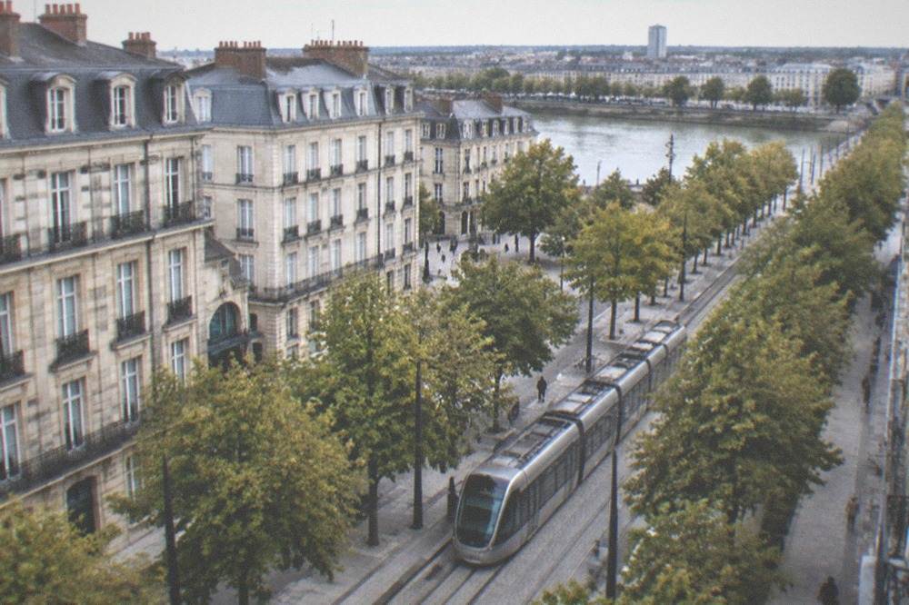 A modern tram travelling along a tree-lined street in central Nantes on a bright afternoon