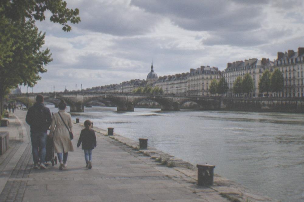 A family walking along a riverside quay in Nantes with a historic stone bridge spanning the water behind them