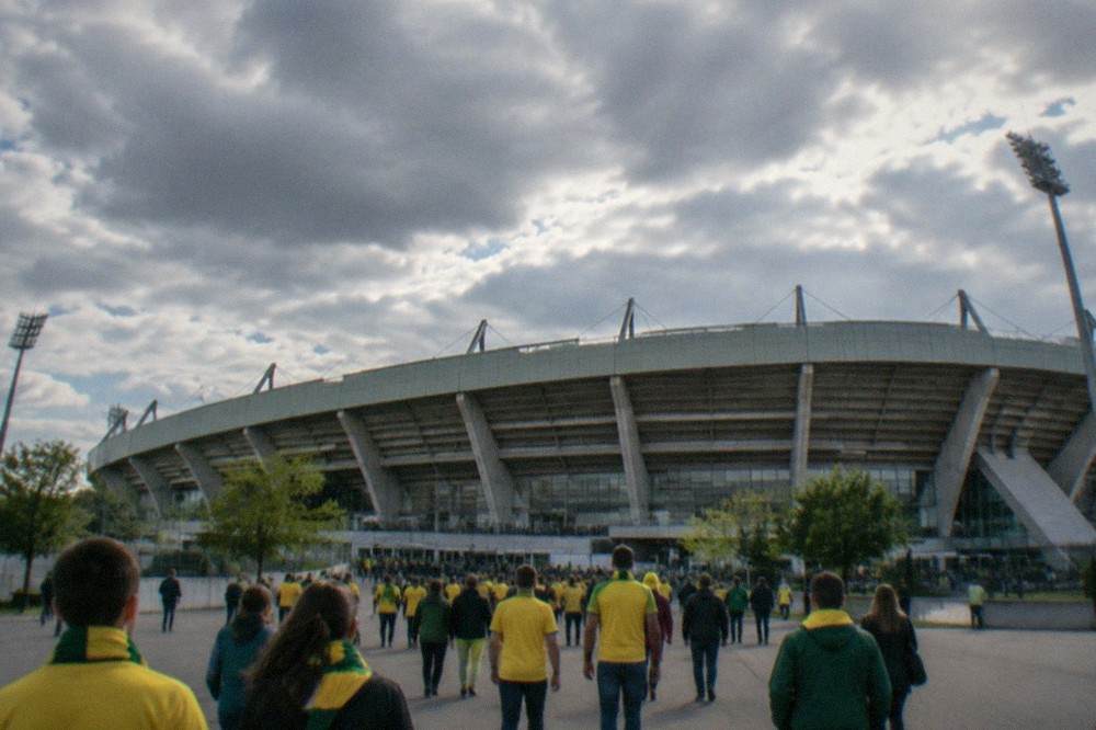 Football supporters in yellow and green walking together toward stadium entrances on a match day