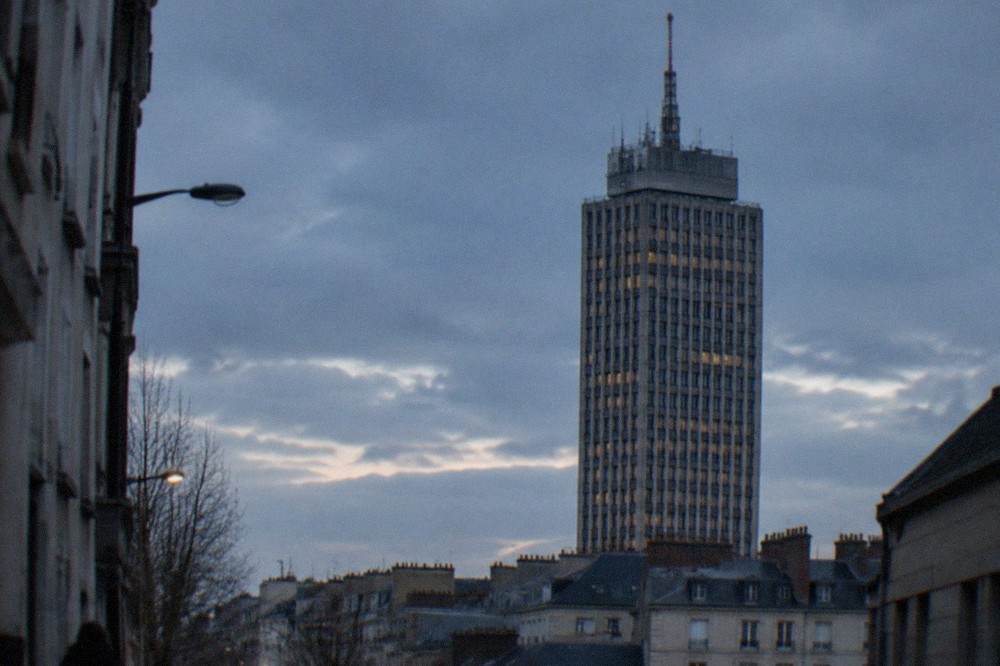The upper floors and antenna of a high-rise tower seen from a Nantes street below