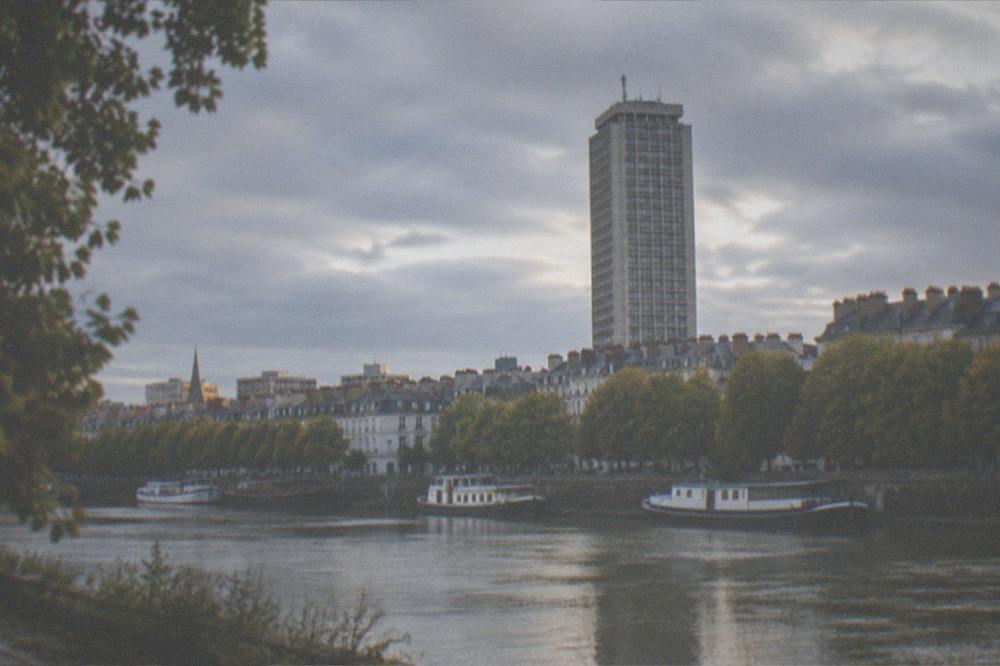 A calm river lined with trees and moored boats seen from a bank in Nantes
