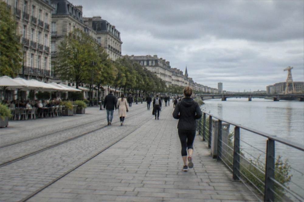 People walking past cafes and restored industrial buildings along a waterfront in Nantes