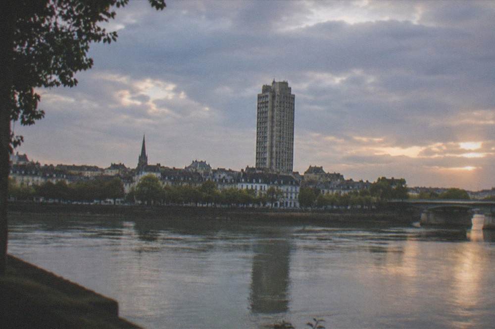 A concrete tower and surrounding city rooftops seen from across a river at dusk