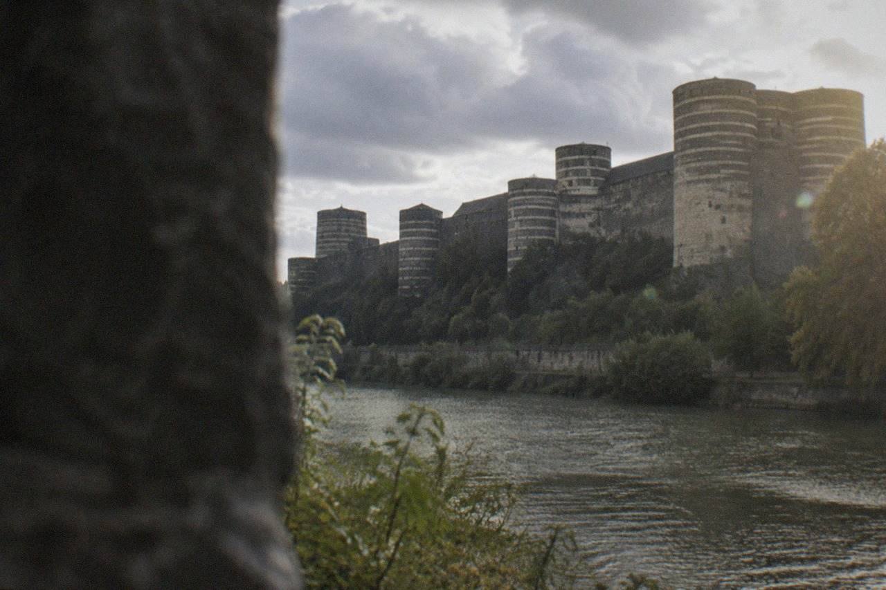 Stone ramparts and towers of a riverside castle rising above trees, seen from the opposite bank