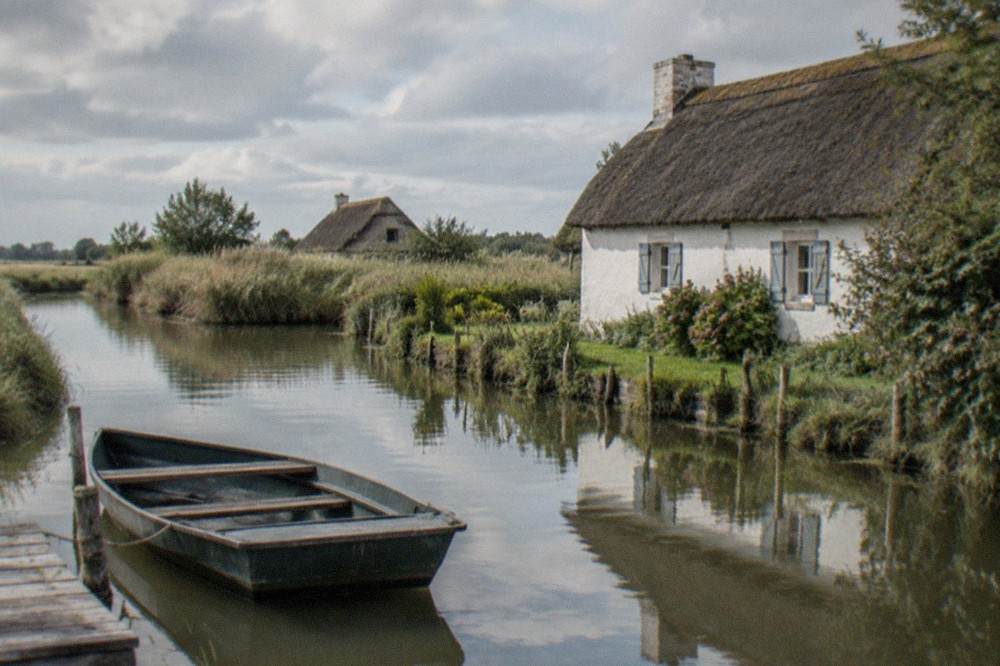 A thatched cottage with whitewashed walls reflected in a calm marsh channel