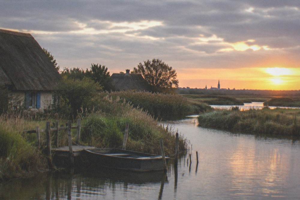 Sunset over a wide marsh with distant church spires on the horizon