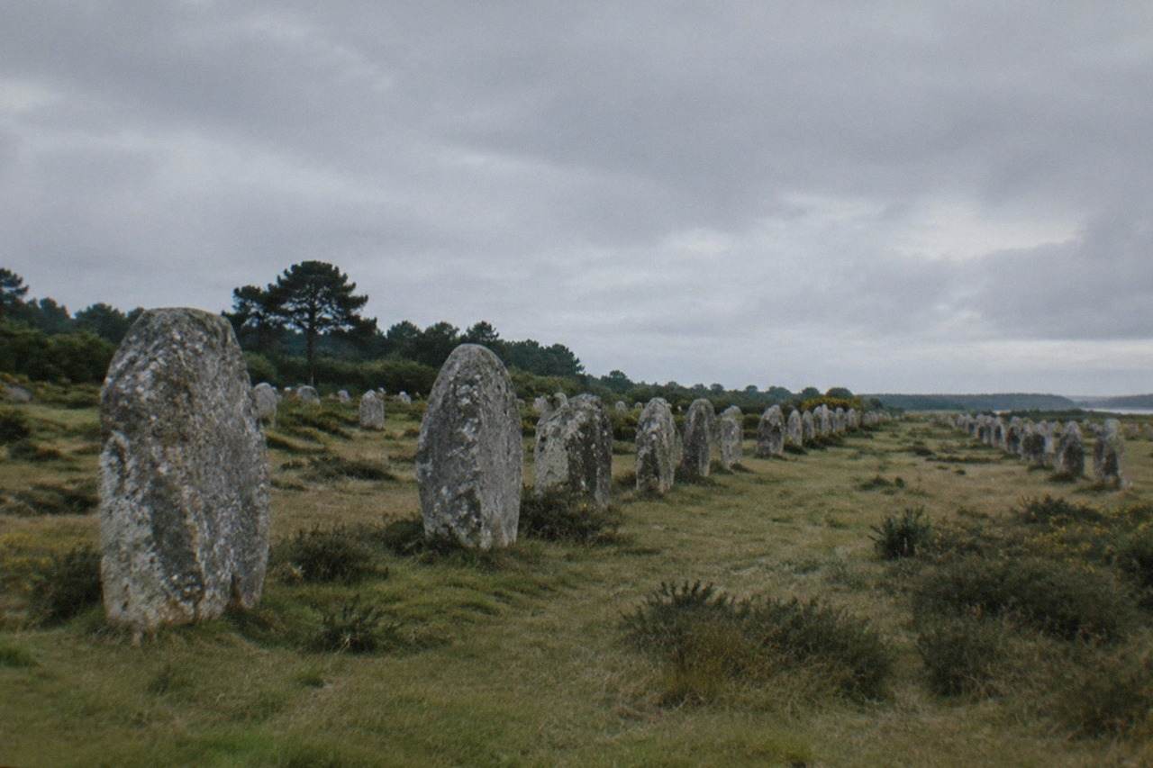 Rows of ancient standing stones stretching across grassy heathland near the Breton coast