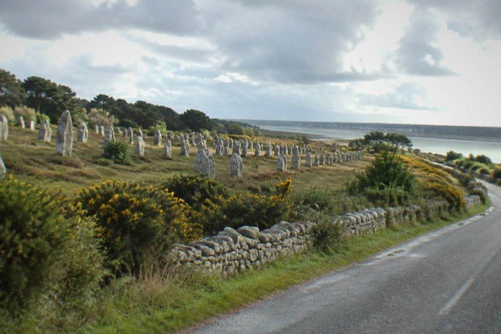 A quiet country road running past low stone walls and gorse toward the Breton coast