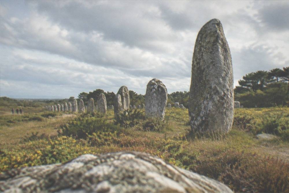 A single tall weathered standing stone silhouetted against a pale coastal sky