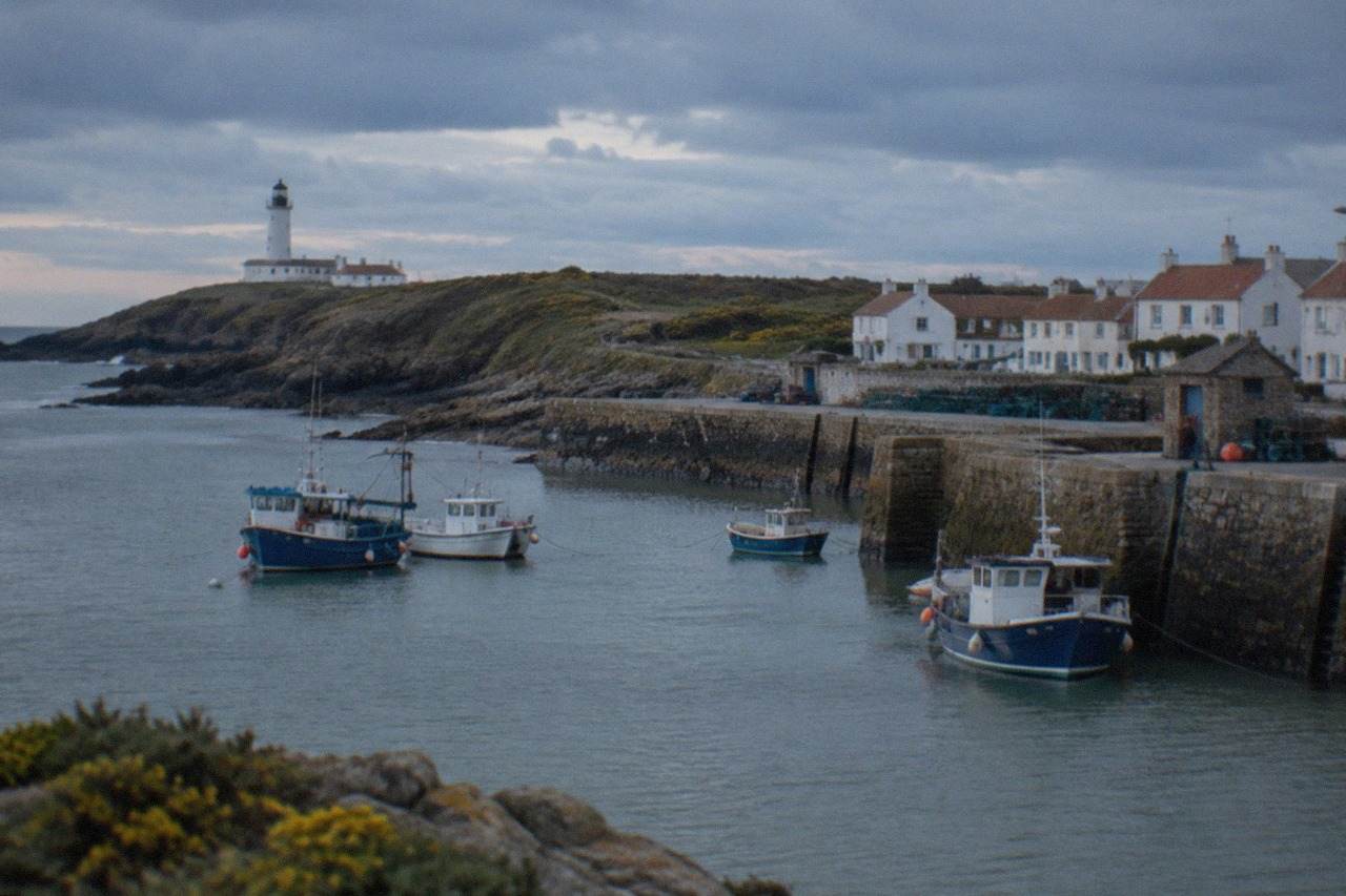 A small Atlantic island harbour with stone quays, moored fishing boats and white houses under a bright sky