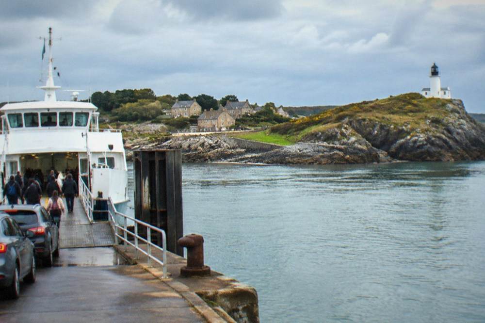 A white ferry at a mainland quay with passengers boarding and cars waiting on the slipway