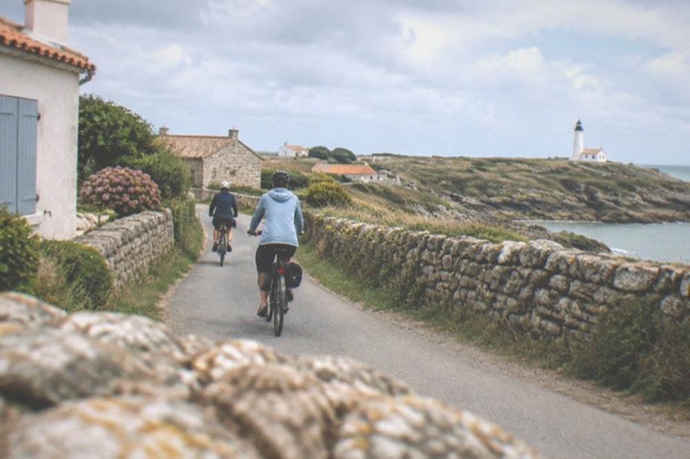 Cyclists on a flat country lane between dry-stone walls and low coastal houses