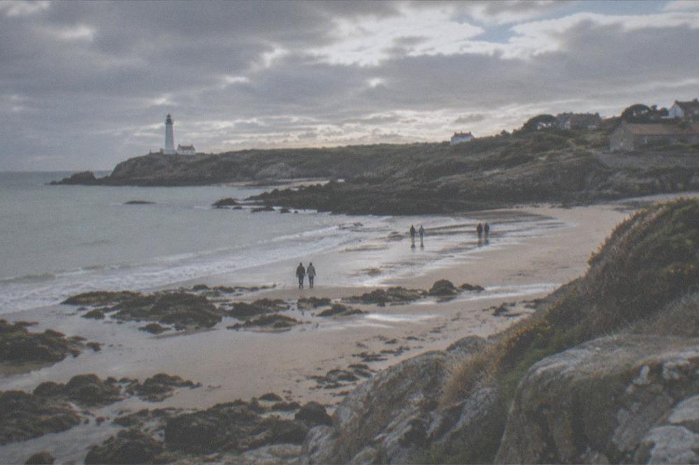 A sandy cove at low tide with rock pools and a few walkers along the waterline