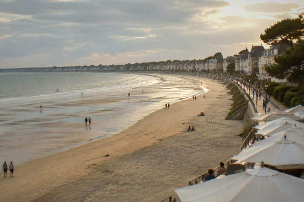 Wide flat sandy beach at low tide with distant bathers and a long promenade lined with parasols