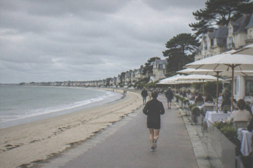 A seaside restaurant terrace with diners at white tablecloths and parasols facing the sea