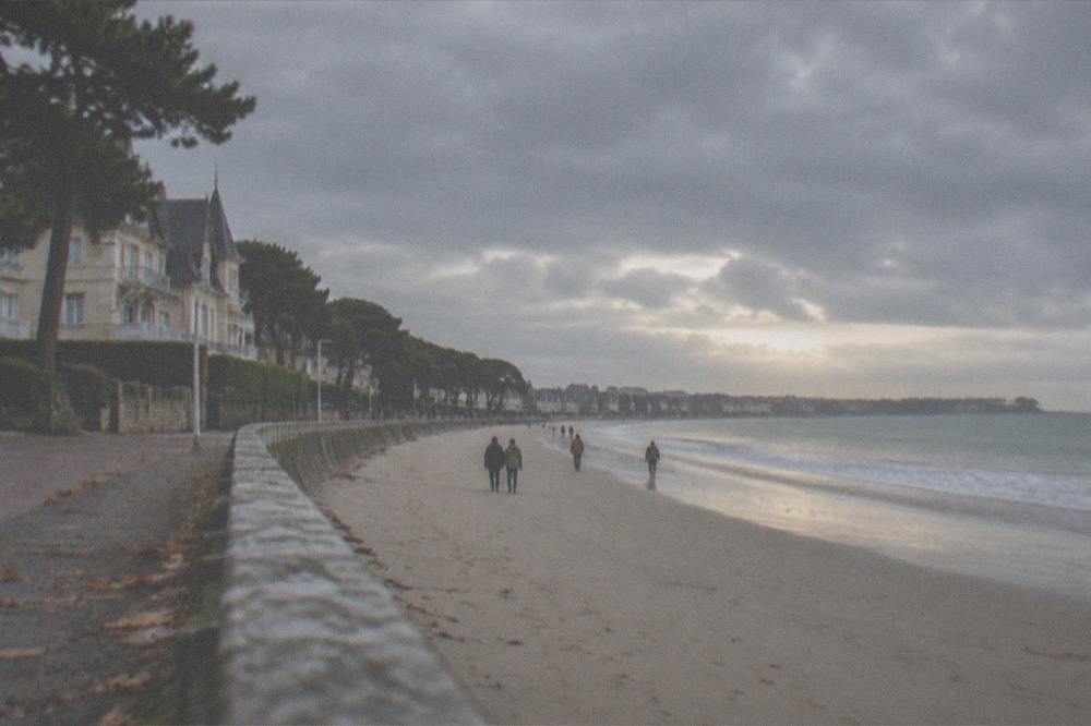 An autumn beach scene with empty sand, low warm light and a few walkers along the waterline