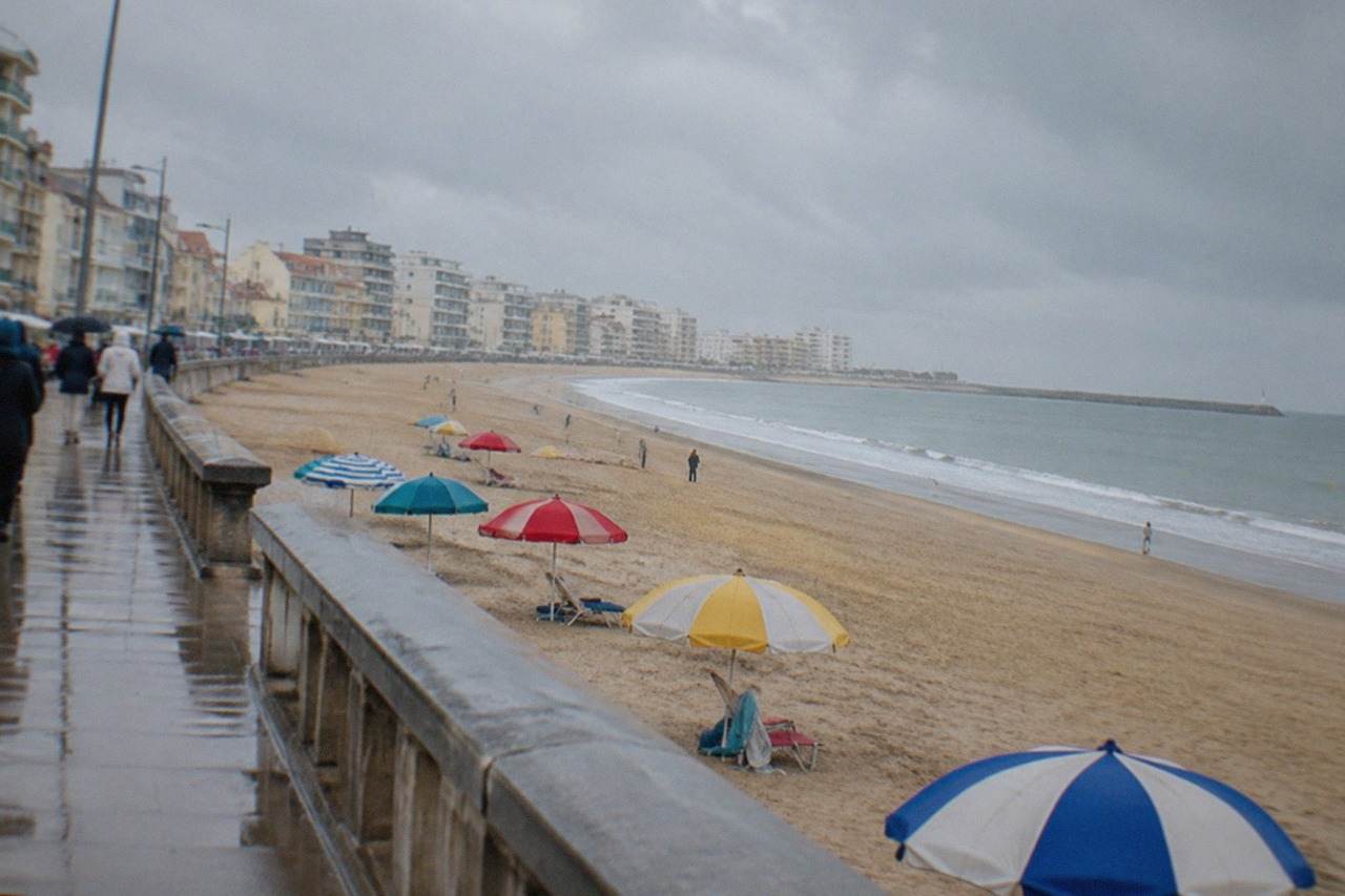 A wide sandy beach beside a seaside promenade with colourful parasols and a calm Atlantic horizon