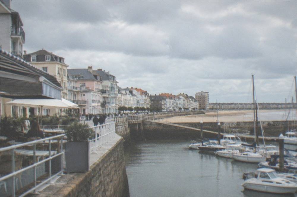 A restaurant terrace with striped awnings overlooking a marina full of yachts