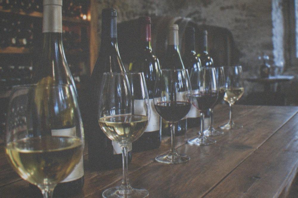 A row of wine bottles and filled tasting glasses on a wooden table in a cellar
