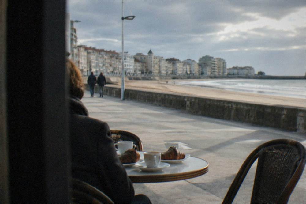A café table beside a promenade with coffee cups and croissants in morning sun
