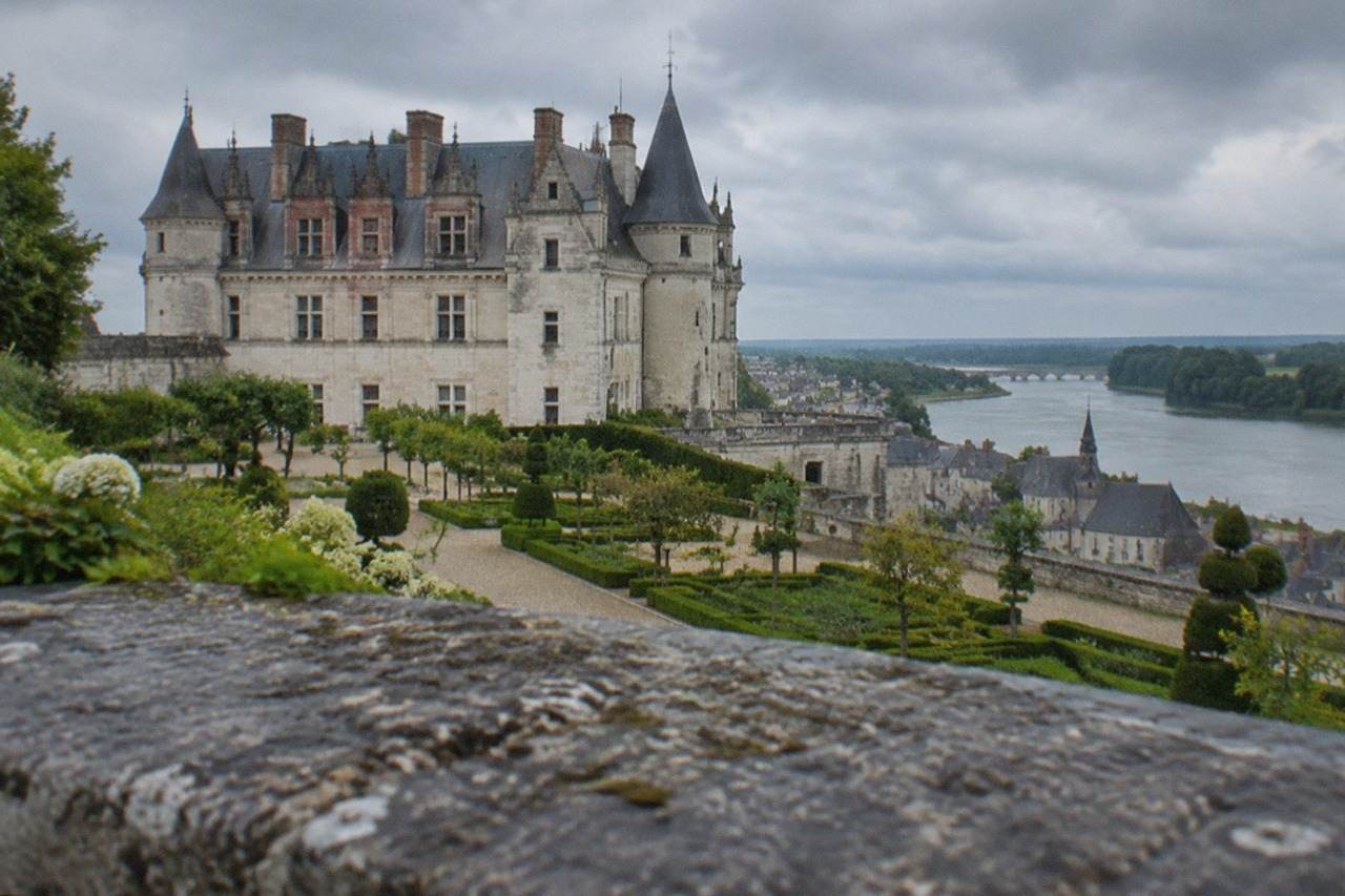 A stone castle with towers rising above a river town in western France