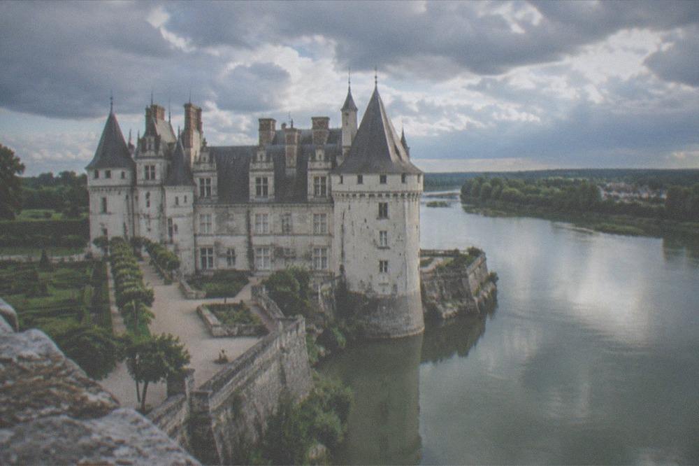 A stone castle keep reflected in a slow green river in late afternoon light