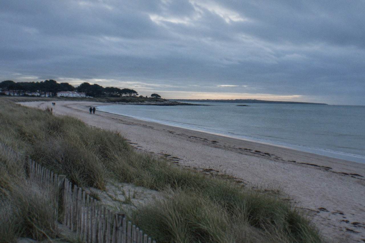 A wide sandy beach on the island of Noirmoutier with pale sand, marram grass and calm Atlantic water