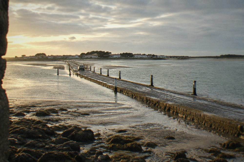 The stone causeway of the Passage du Gois stretching across wet sand toward the island under a wide sky
