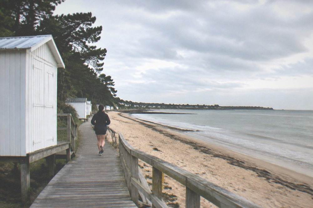 A white wooden bathing cabin and boardwalk above a calm Atlantic beach with pine trees behind