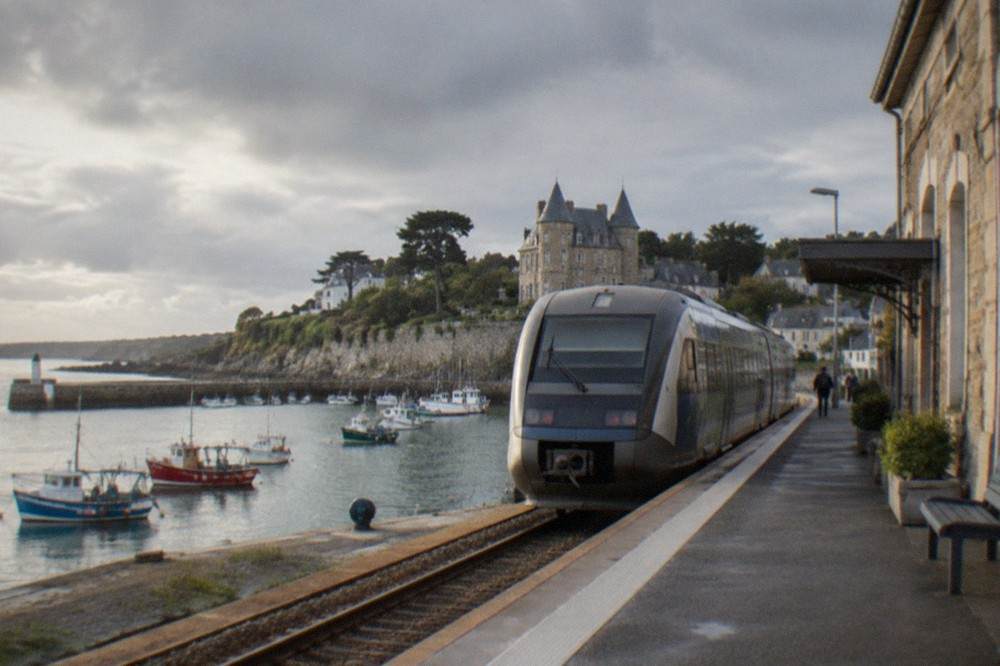 A regional train waiting at a platform beside a stone station building in early morning light