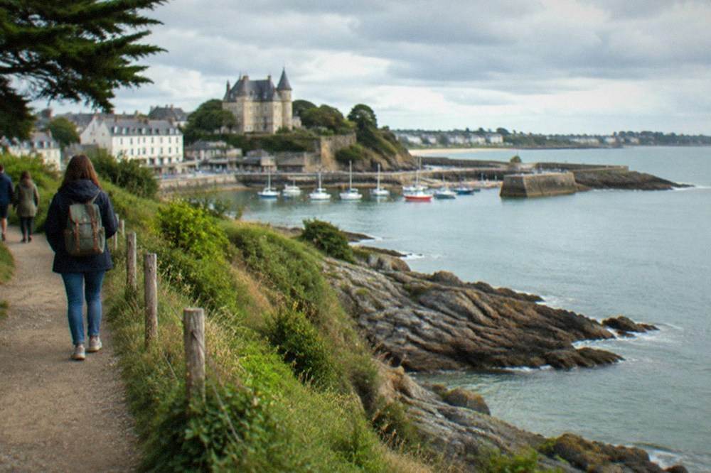 Walkers on a clifftop path above a rocky Atlantic shoreline, with a bay curving away in the distance