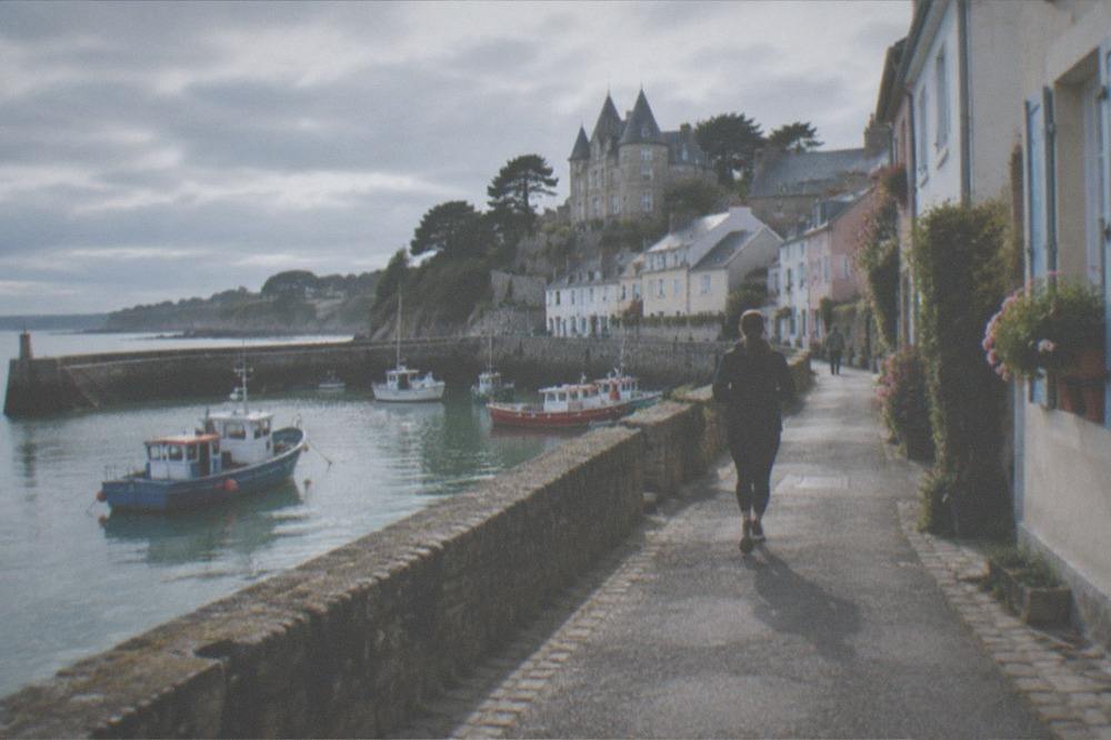Pastel-walled narrow streets climbing a hillside above a harbour, with shutters and flower boxes on the houses