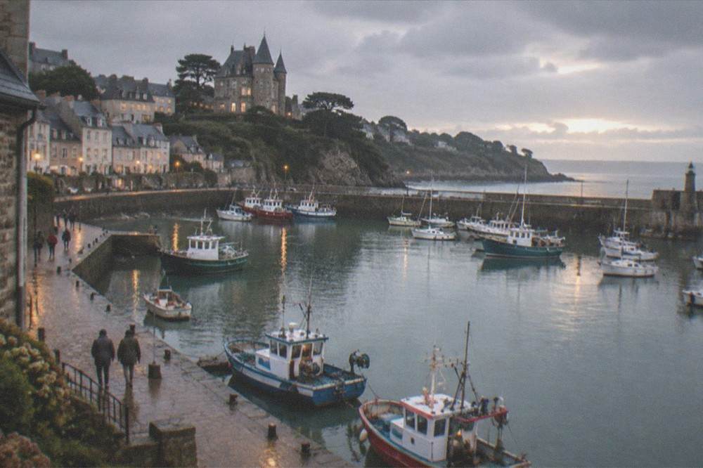 Evening light across a small Atlantic harbour, with the day's last walkers on the quay and lights beginning to show in windows above