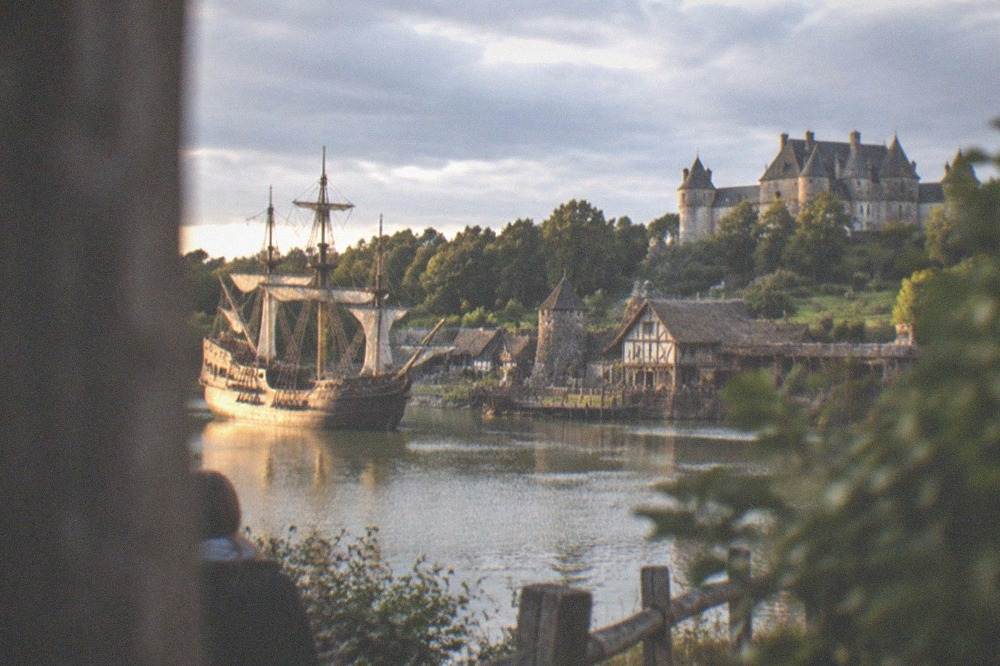 A lakeside stage set with a full-rigged sailing ship and illuminated evening sky