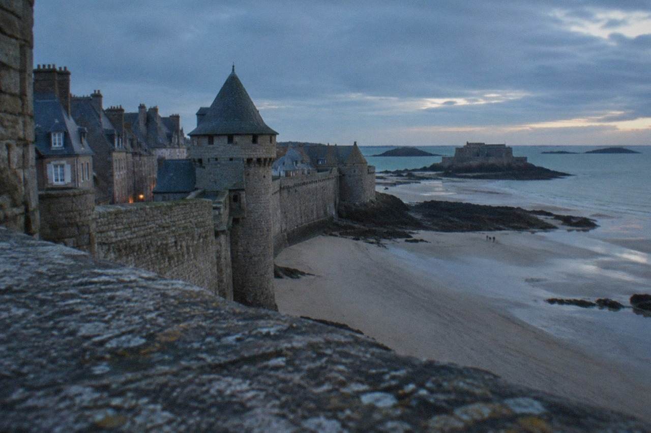 Granite walls and towers of a fortified Breton port town above a wide sandy beach at low tide